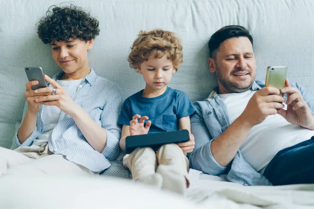 a man, woman and child sitting on a couch looking at their cell phones